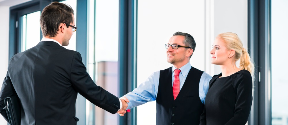 interview ends and man and woman offer man the job - dressed in business attire shaking hands