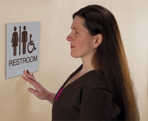 woman who is blind is seen touching the braille embossed on an accessible washroom sign