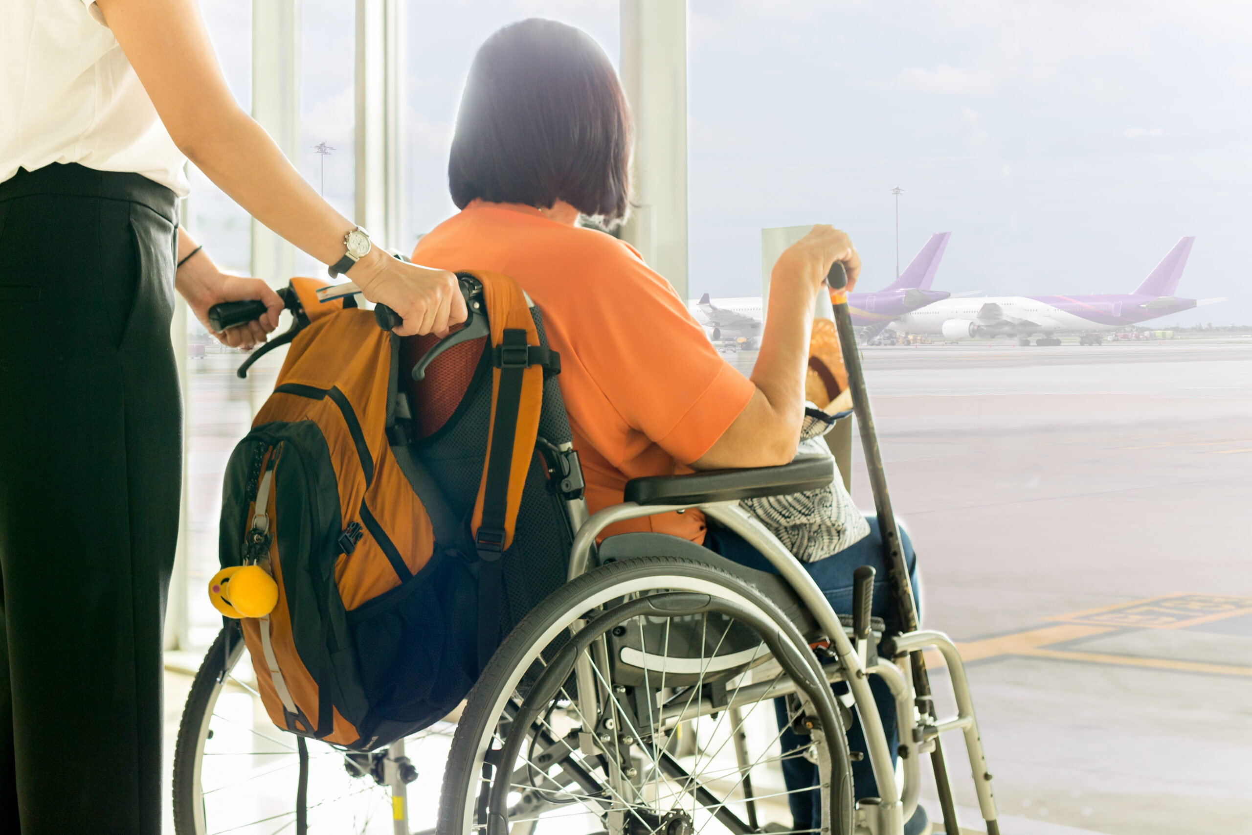 Support person with an old traveller with disability in wheelchair waiting for boarding at International airport