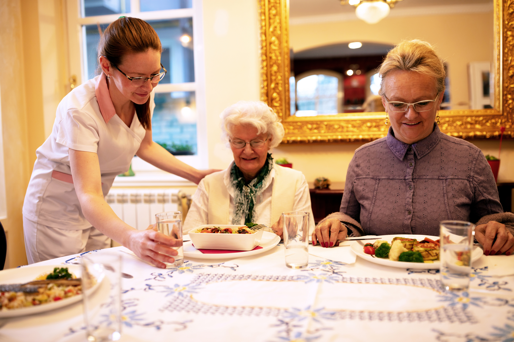 Caring nurse serving meals for dinner and attending people in a retirement home