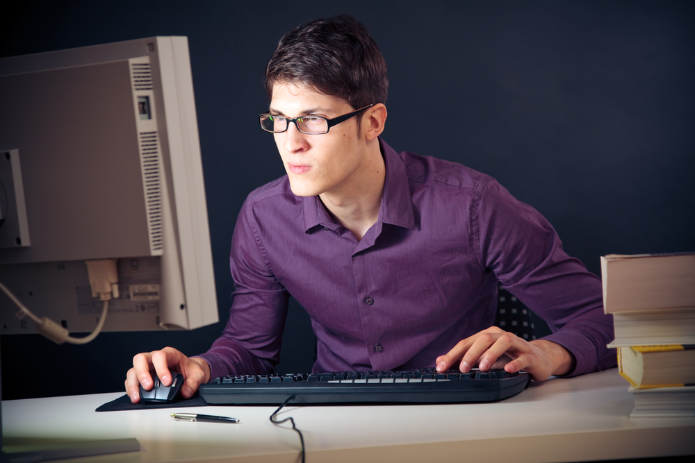young man with glasses sitting in front of his computer