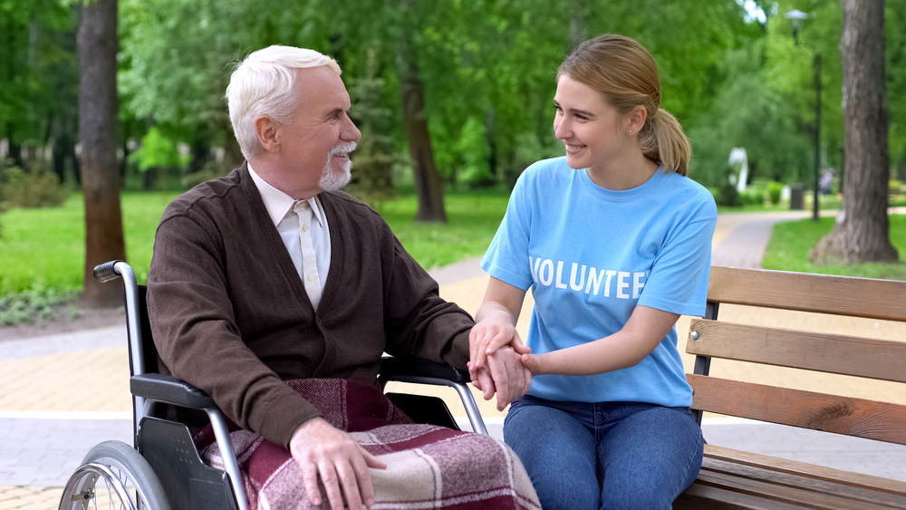 Kind young woman volunteer t-shirt holding disabled male hand, patient support