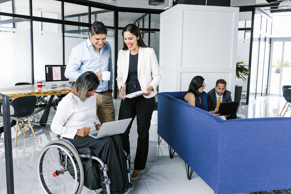 a woman in wheelchair working with coworkers using computer