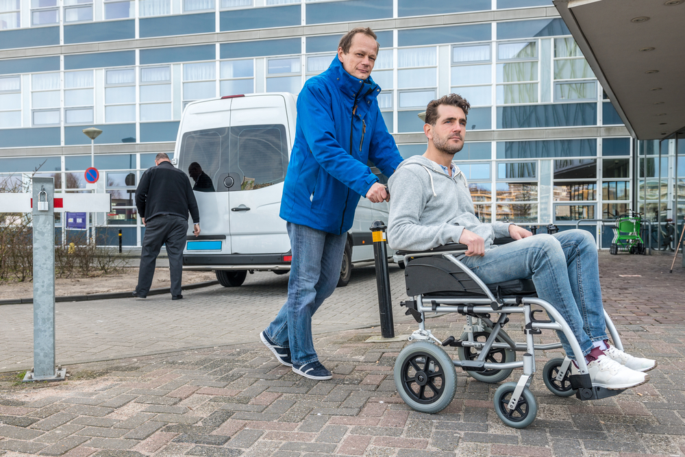 Man Pushing Son On Wheelchair With Taxi In Background